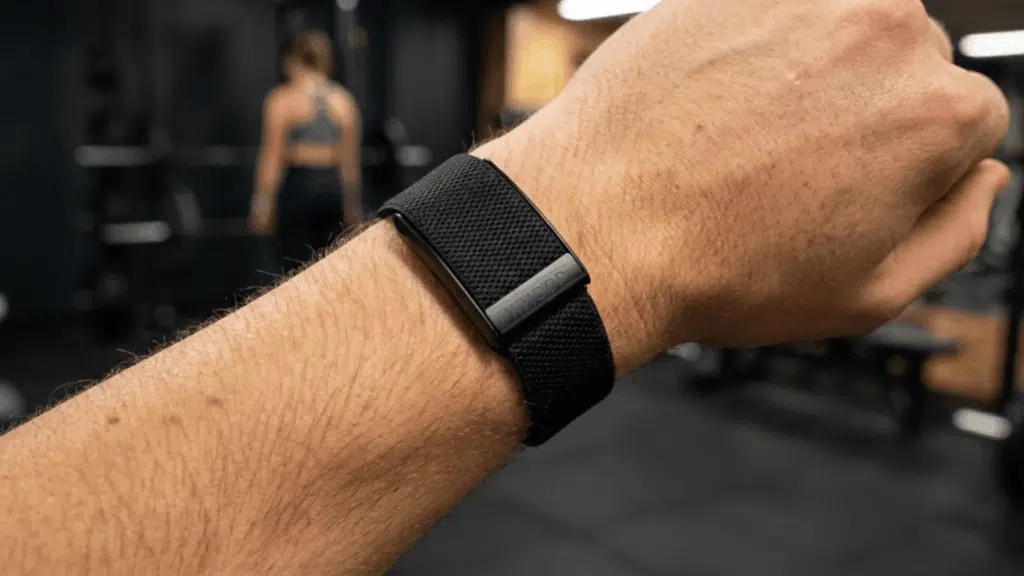 close-up of a person wearing a Whoop fitness band on wrist in a gym setting, highlighting its sleek, screen-free design and strap fit