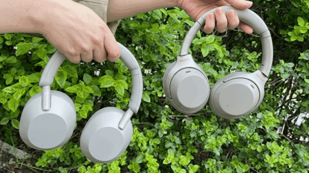 person holding Sony WH-1000XM5 and WH-1000XM4 wireless noise-canceling headphones outdoors, showing the design difference between both models.