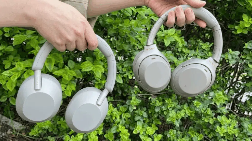person holding Sony WH-1000XM5 and WH-1000XM4 wireless noise-canceling headphones outdoors, showing the design difference between both models.