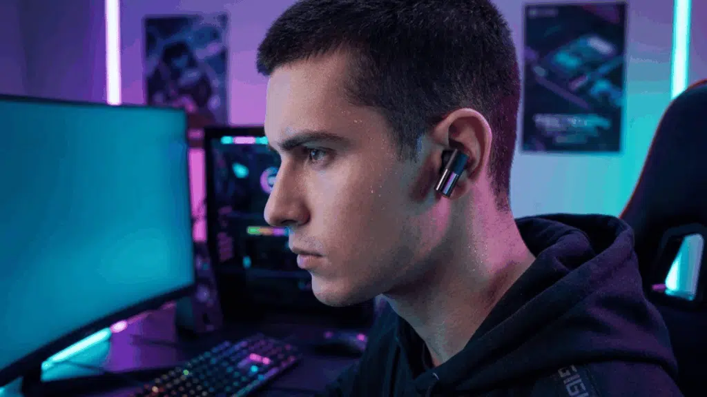 person wearing wireless earbuds while gaming on a PC setup with RGB lighting, showing focus and low-latency audio use