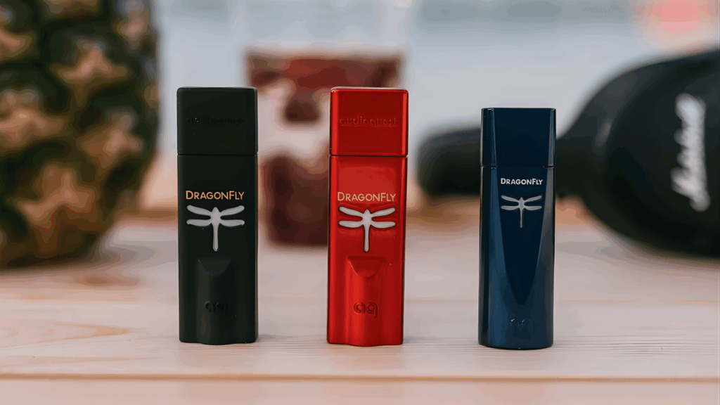 three sleek dragonfly usb dacs in red, black, and blue colors are displayed against a vibrant, wavy neon background.
