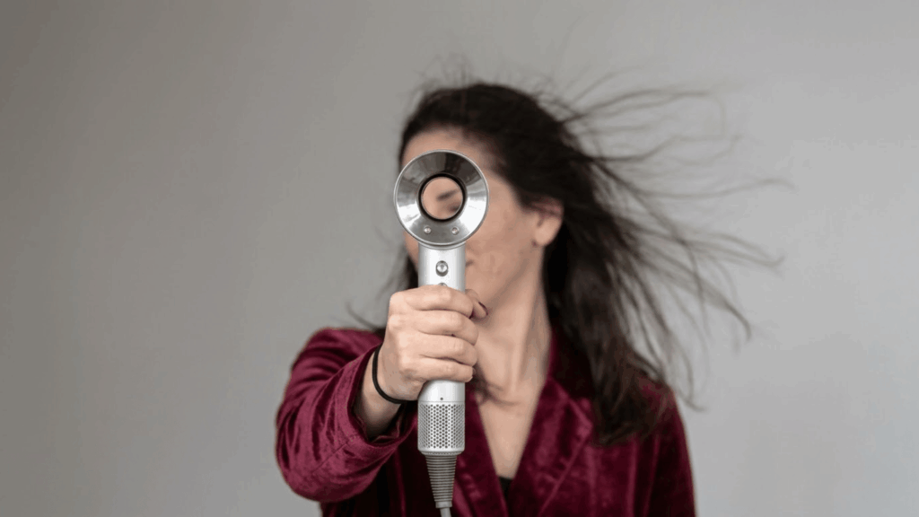 woman using a Dyson Supersonic hair dryer with airflow blowing her hair back, showing the hollow nozzle design