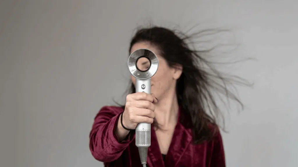 woman using a Dyson Supersonic hair dryer with airflow blowing her hair back, showing the hollow nozzle design