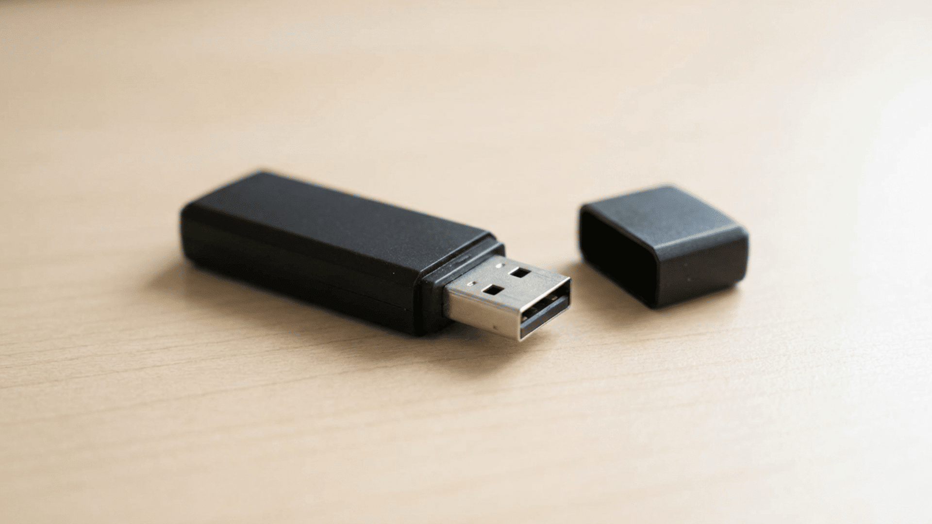 black USB flash drive with cap removed placed on a wooden surface, showing the connector and compact portable storage design.