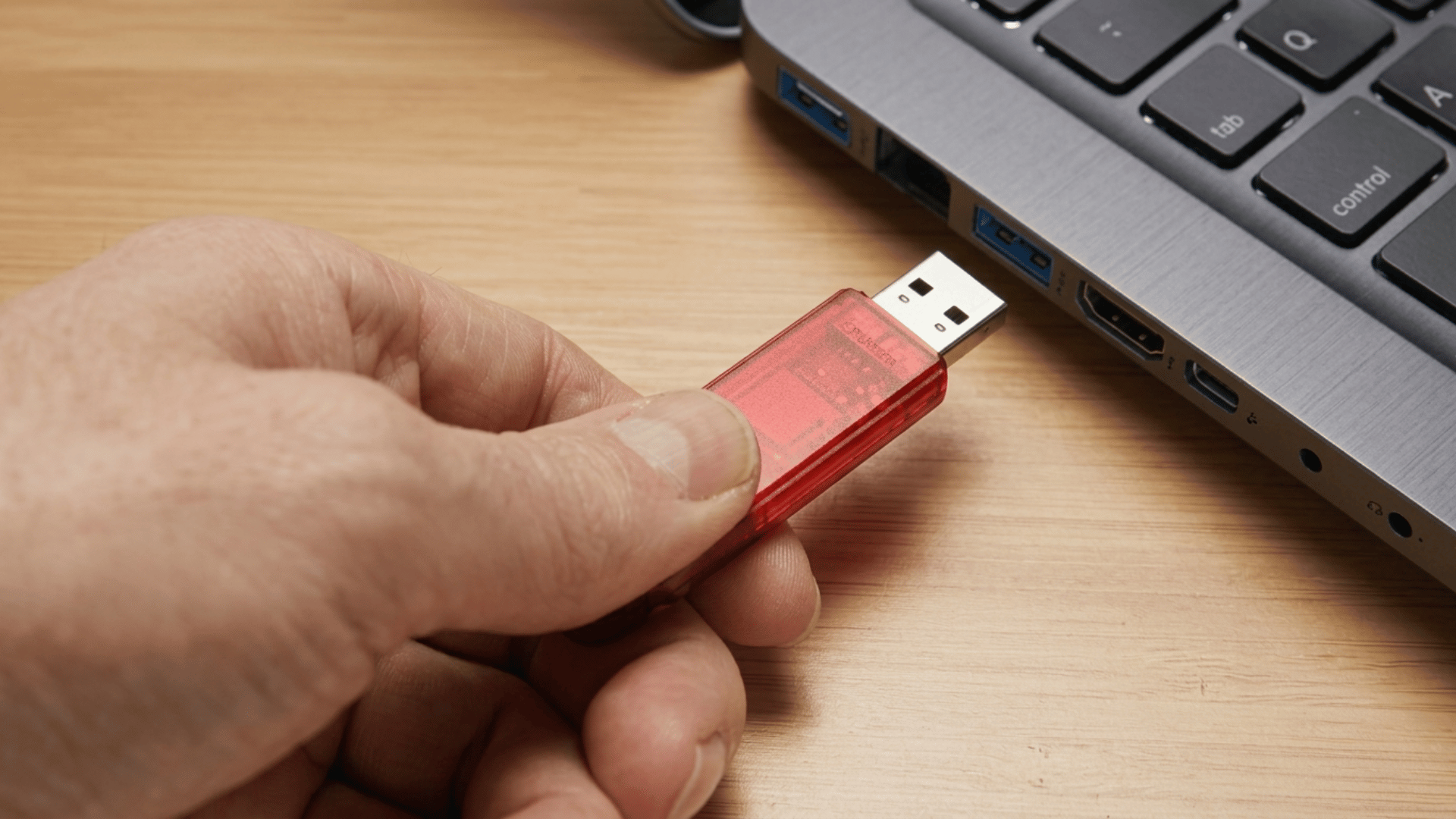 hand inserting a red USB flash drive into a laptop port, demonstrating how a portable storage device connects for data transfer.