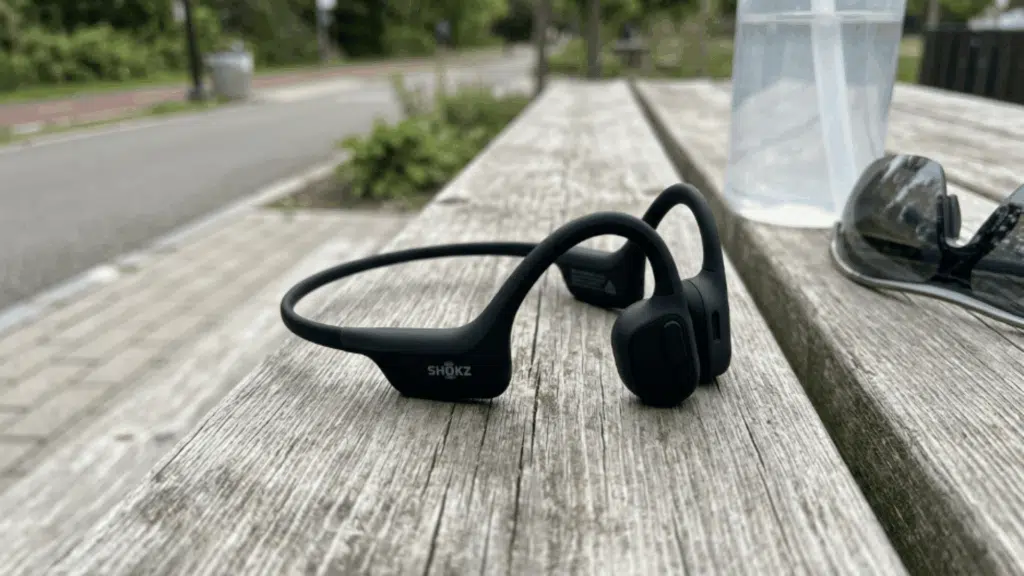 shokz OpenMove bone conduction headphones placed on a wooden bench outdoors, showing design suited for fitness and outdoor use