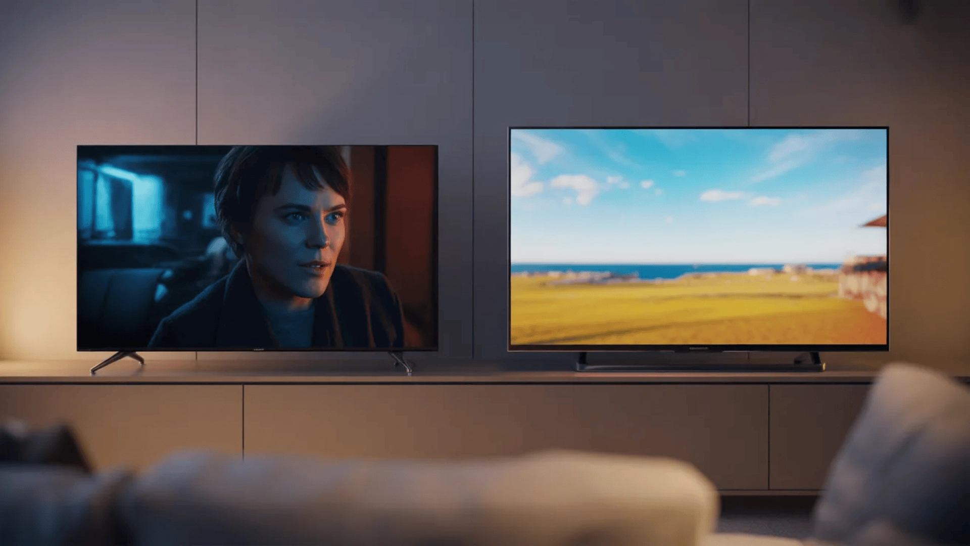 Two flat-screen TVs side by side showing dark and bright scenes in a living room