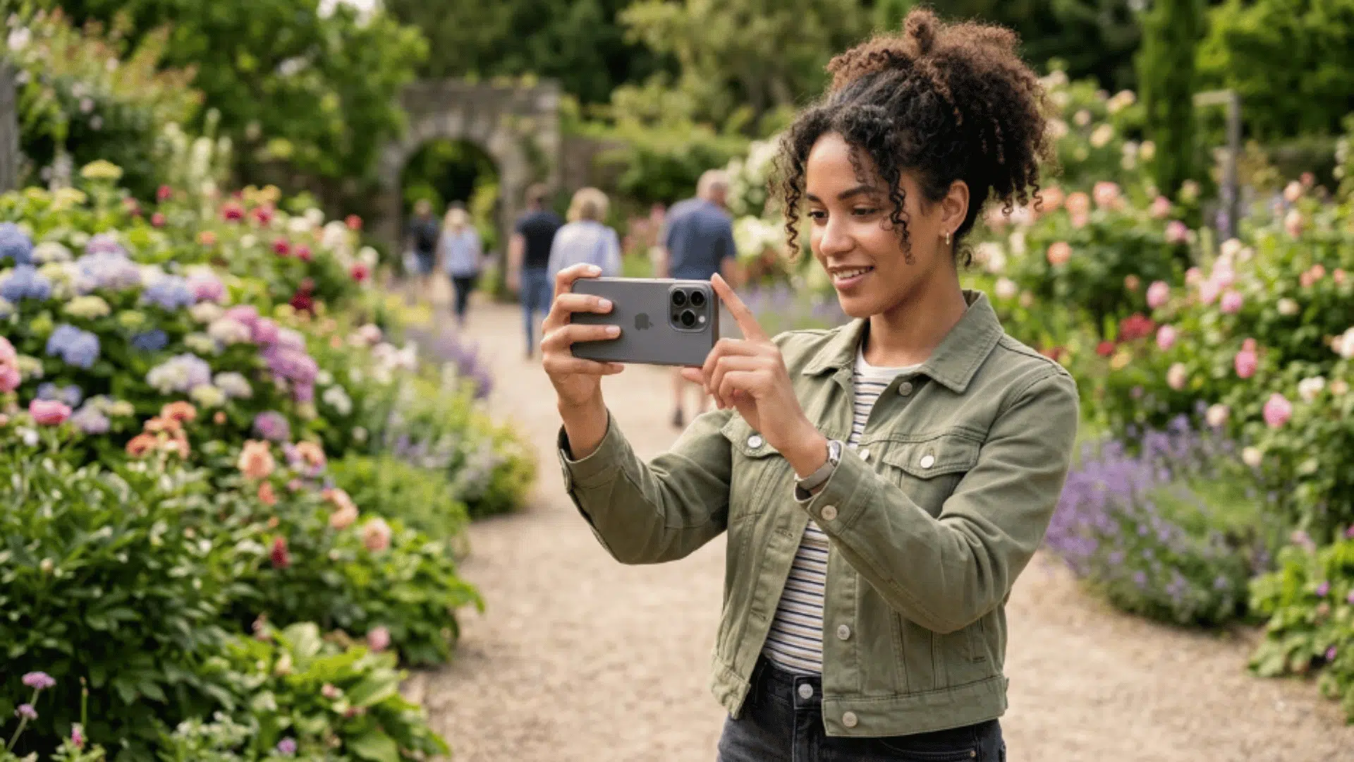 woman taking photo outdoors with iPhone 16 Pro camera, capturing vibrant garden scene with natural lighting and sharp detail.