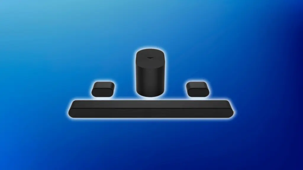 Black home audio system with a long soundbar, cylindrical subwoofer, and two compact satellite speakers, arranged on a light blue background.