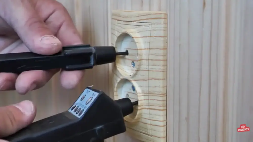 Hand using a tester device on a wooden wall electrical outlet with two sockets