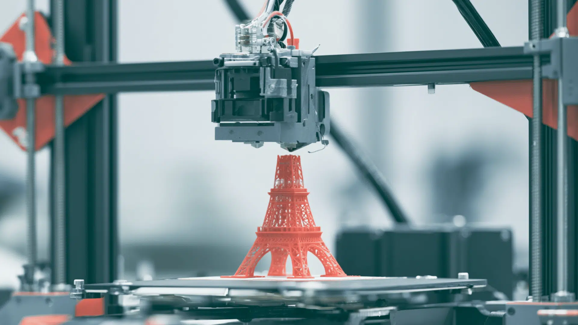 a 3d printer in an indoor setting printing a 3d tower structure in red color blurred grey background