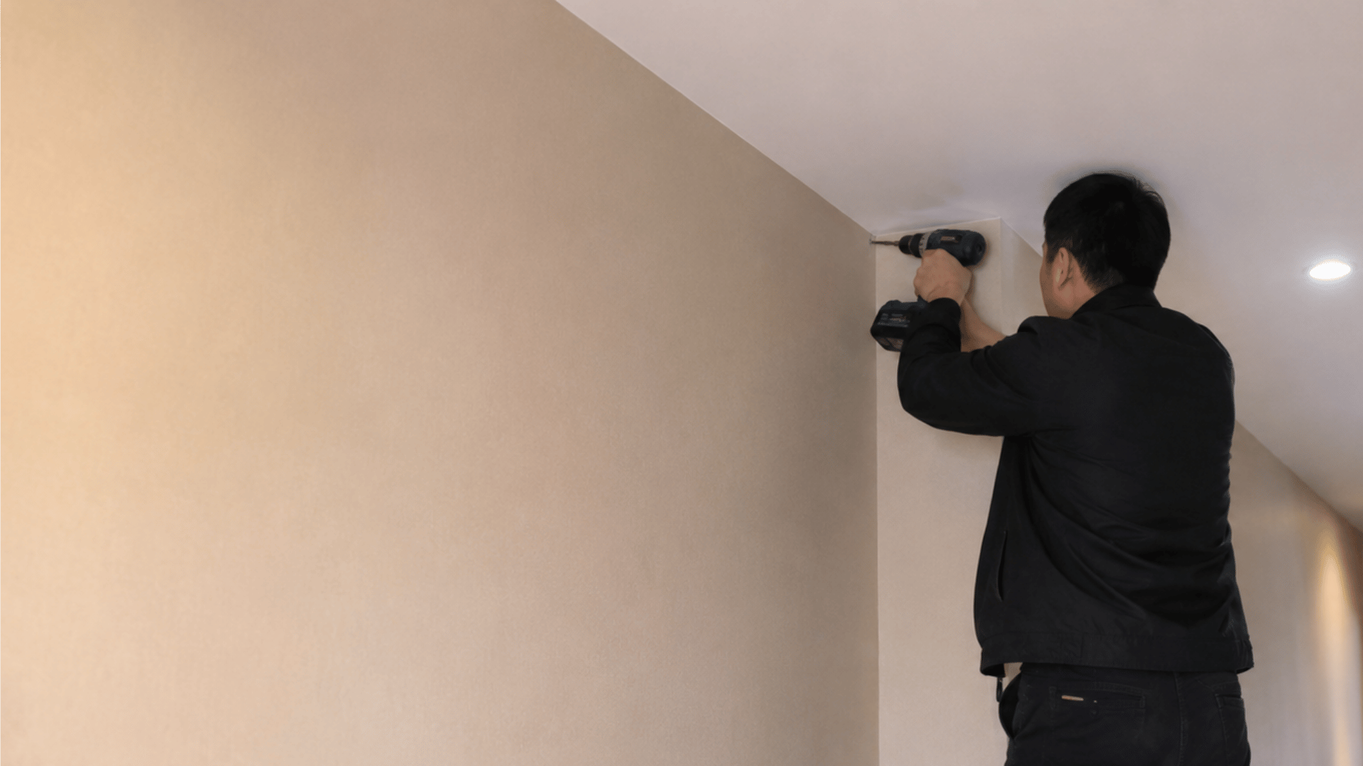 a handyman drilling in corridor space standing on a ladder showing the process of cctv camera installation