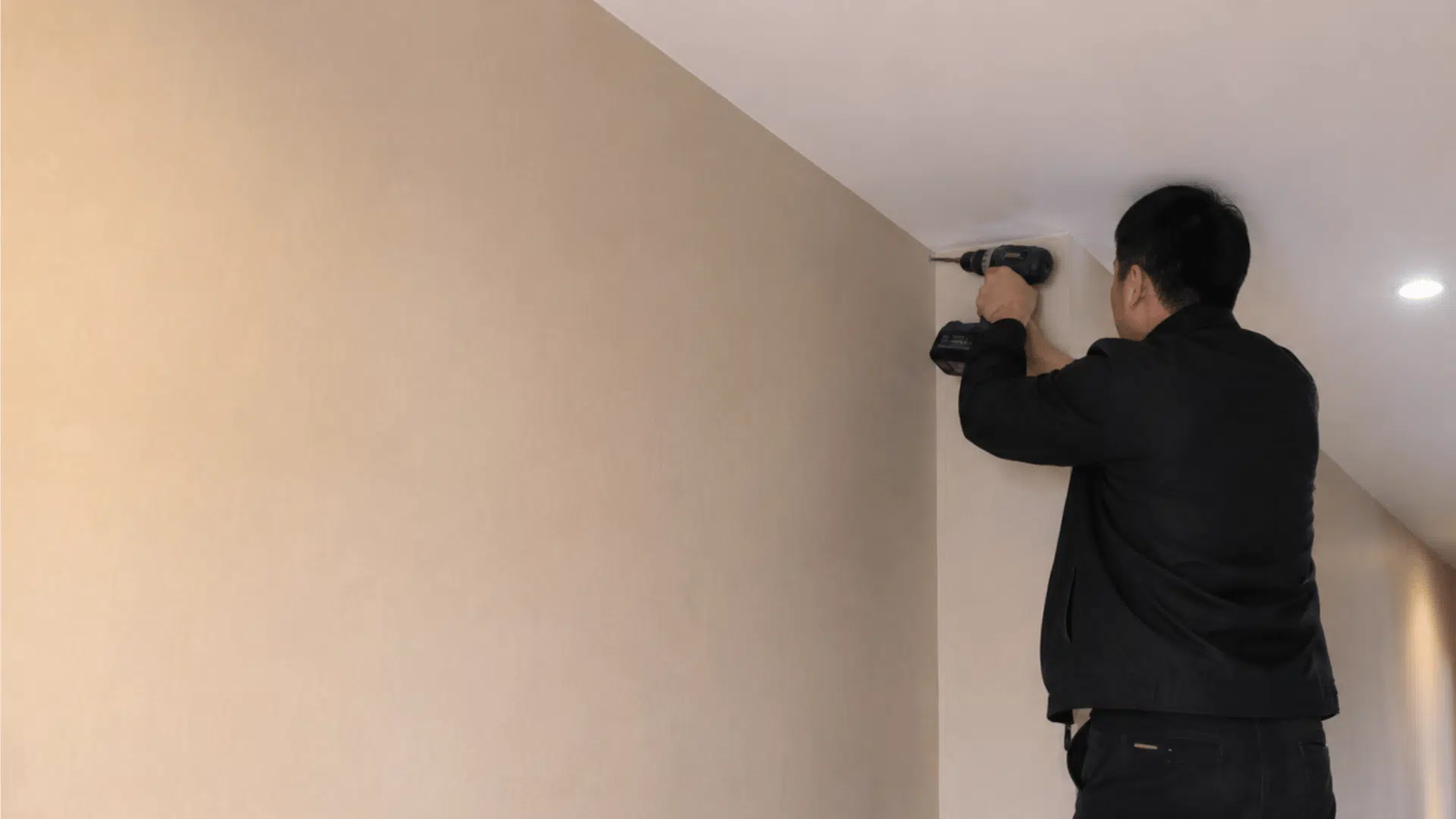 a handyman drilling in corridor space standing on a ladder showing the process of cctv camera installation