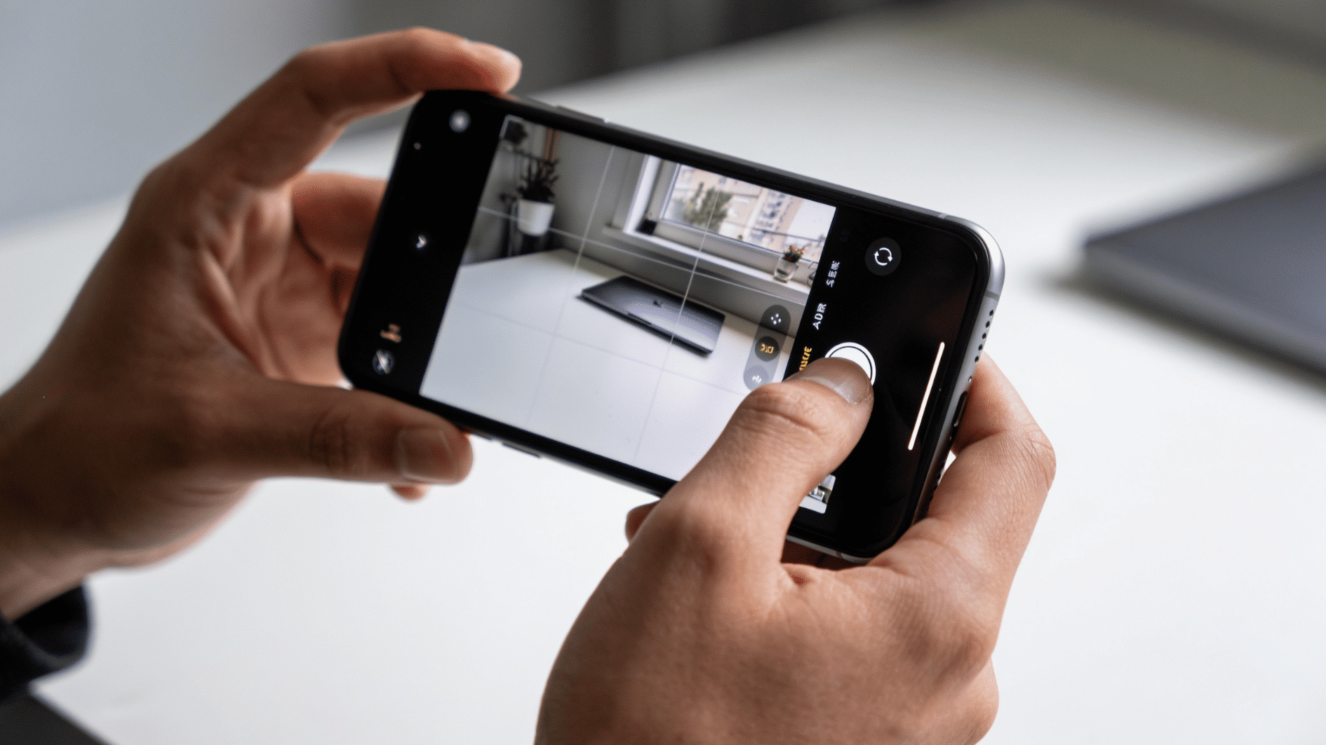 a person holding an iphone with the camera app open in a quiet indoor setting, one hand adjusting silent mode on the side of the phone