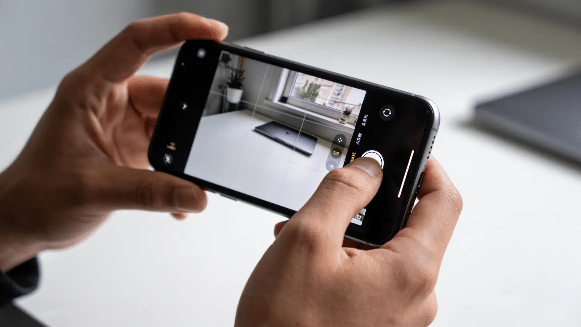 a person holding an iphone with the camera app open in a quiet indoor setting, one hand adjusting silent mode on the side of the phone