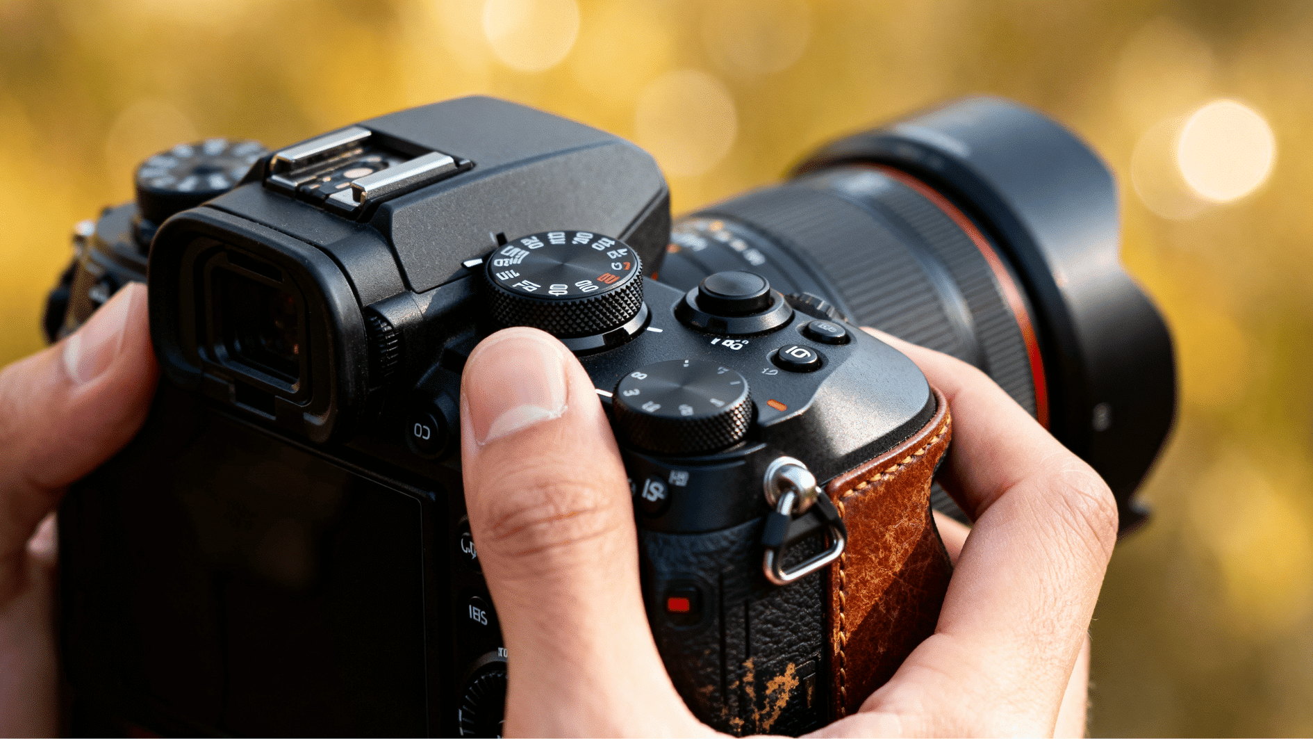 close-up of hands adjusting manual controls on a dslr camera with a blurred outdoor background and warm lighting.
