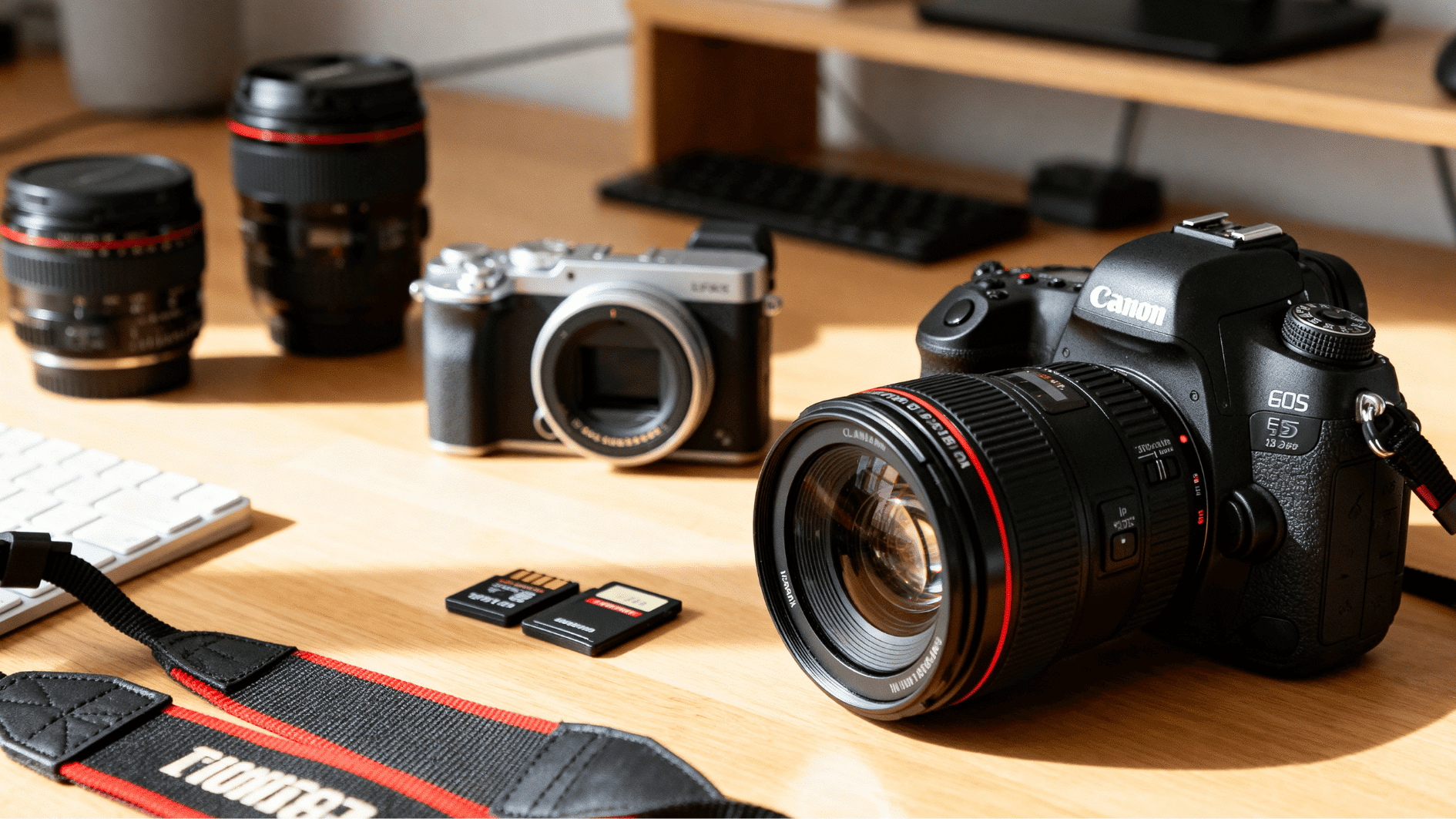dslr and mirrorless cameras placed on a wooden desk with lenses and memory cards in a bright studio setup.