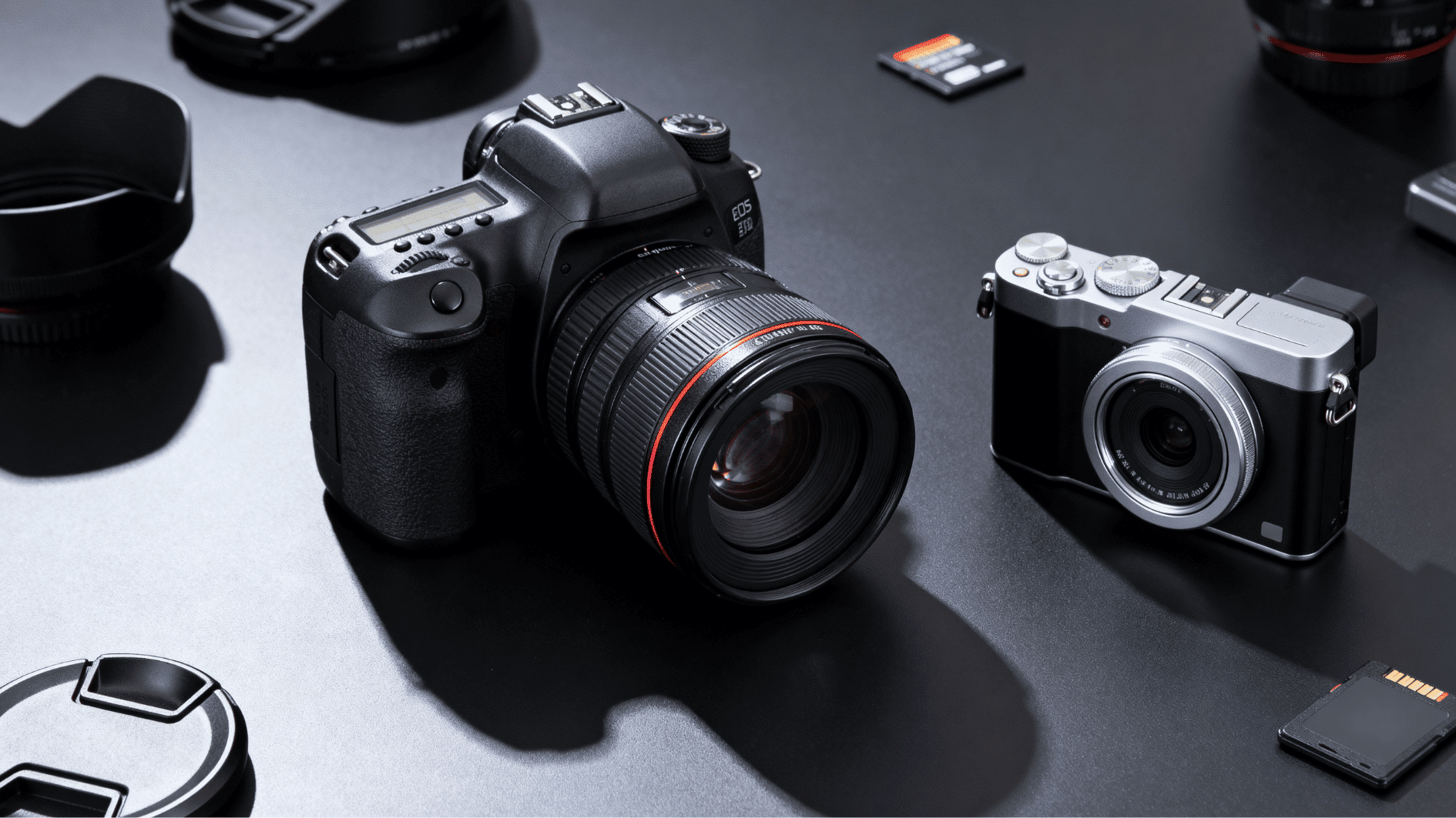 dslr and mirrorless cameras placed side by side on a dark desk with camera lenses and memory cards in a studio setup.