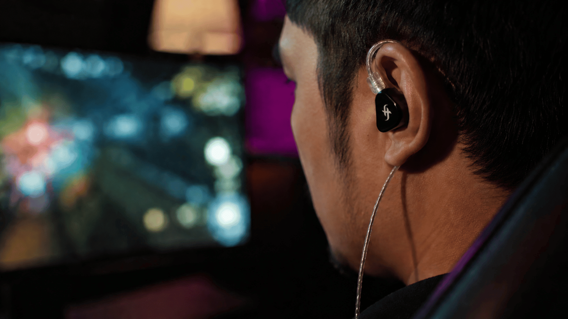 gamer playing game blurred tv screen with ambient glow ear closeup of simgot ea500lm wired earphones with simgot logo visible on it
