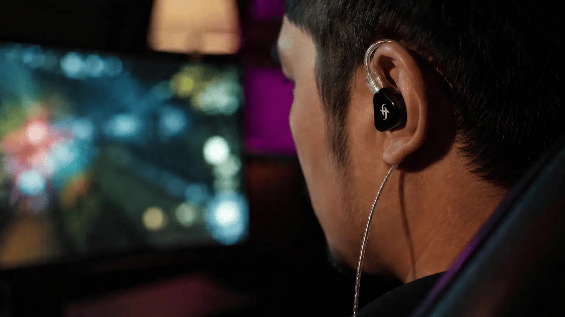 gamer playing game blurred tv screen with ambient glow ear closeup of simgot ea500lm wired earphones with simgot logo visible on it