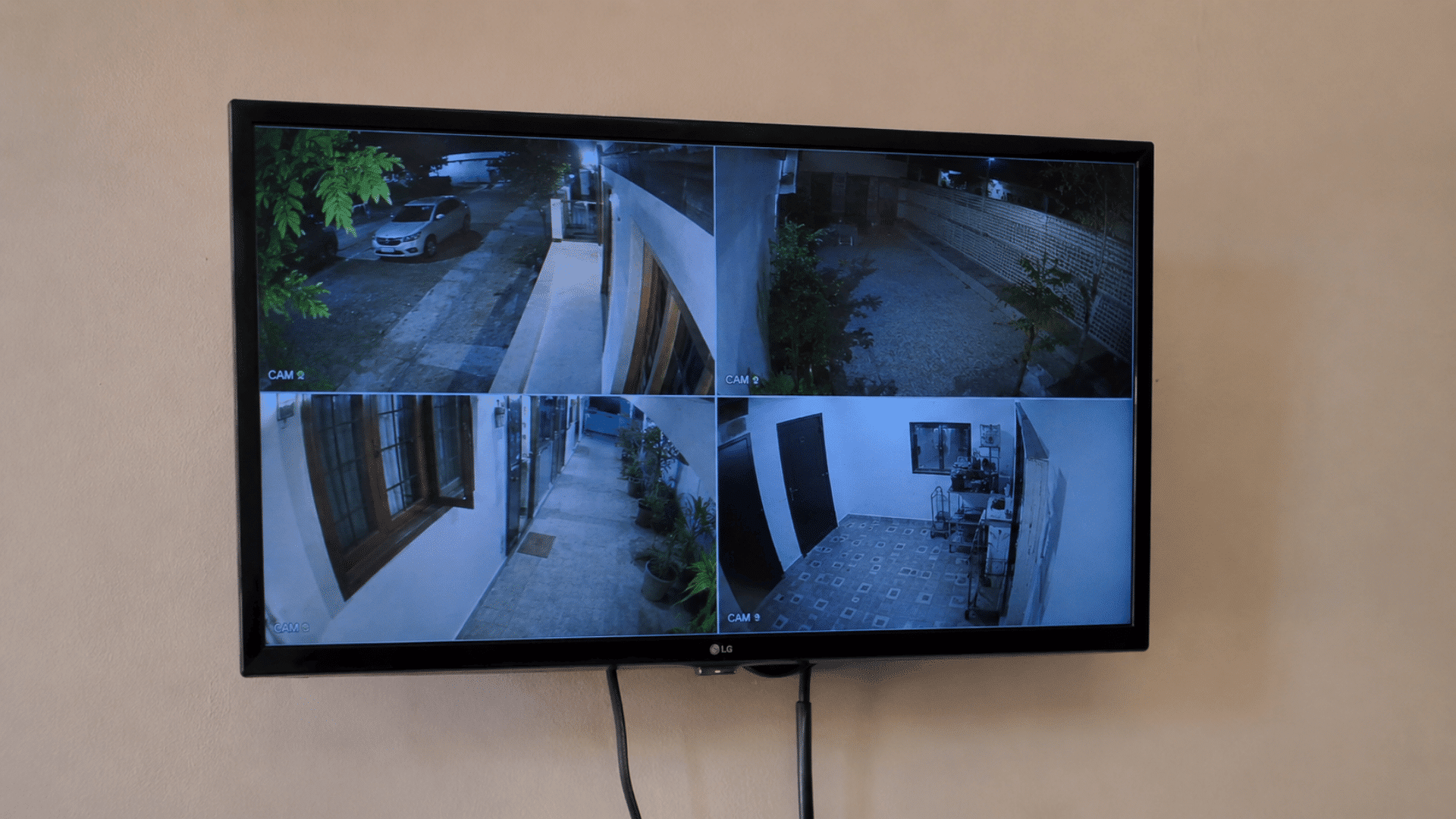 wall mounted home security cctv setup with multi-view monitor showing different areas of the house off white background wall and tv branding visible
