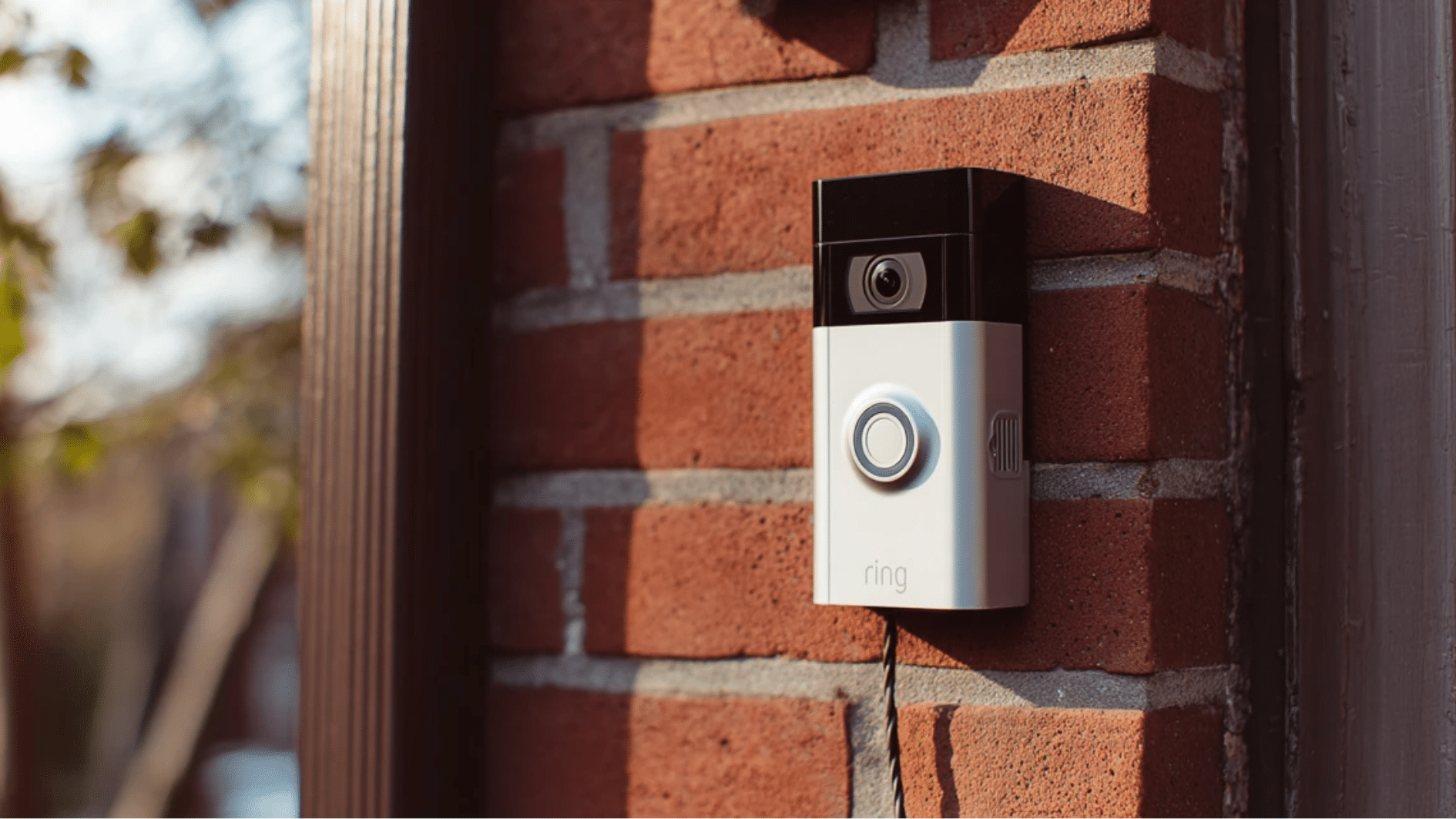 white ring video doorbell installed on a red brick wall beside a front door with wiring connection visible at the base of the device (1)