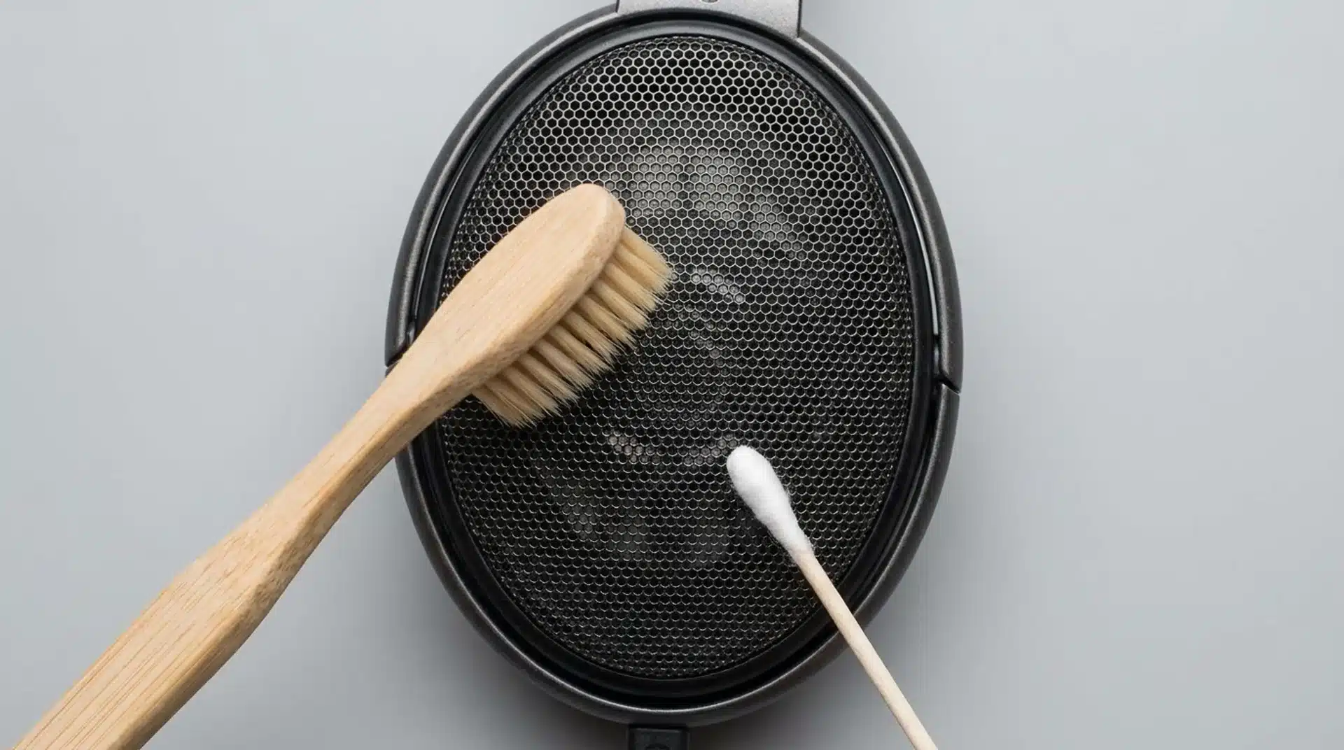 Headphone mesh grille being gently brushed with a dry toothbrush and cleaned along the rim with a dry cotton swab.