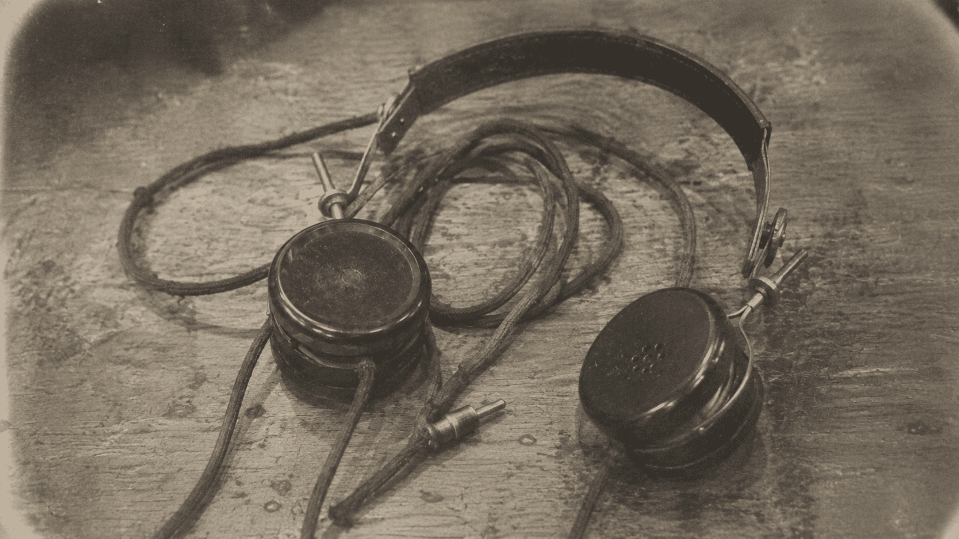 early radio headphones from the 1910s with cloth-covered wires resting on a worn wooden table