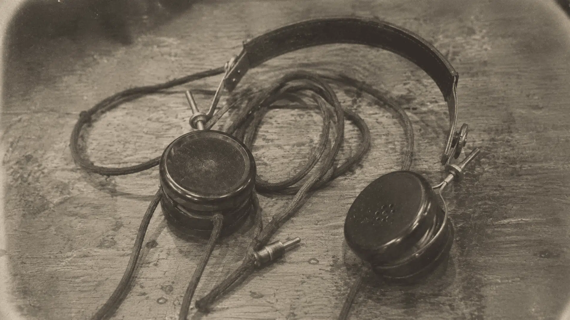 early radio headphones from the 1910s with cloth-covered wires resting on a worn wooden table
