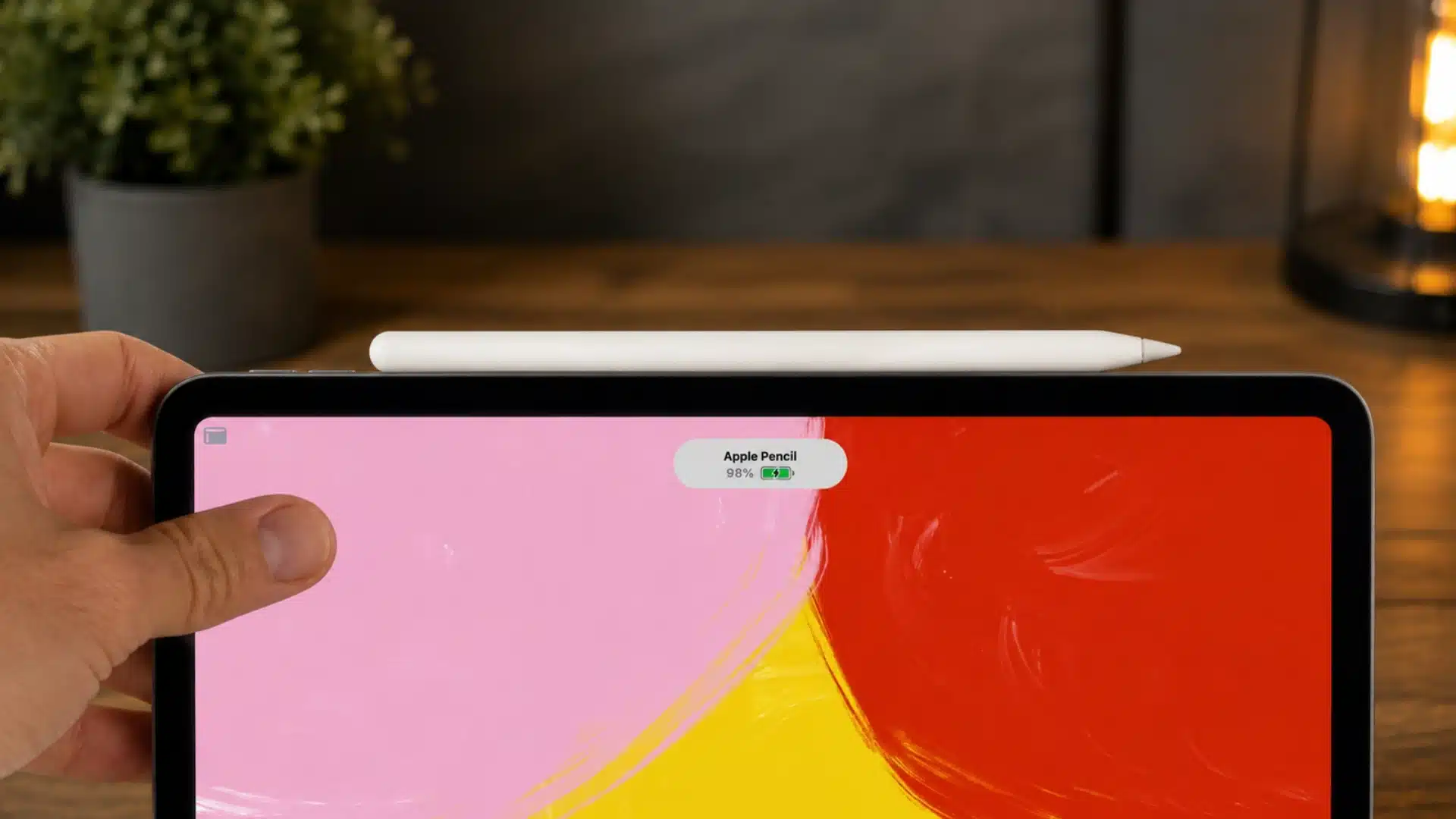 Apple Pencil magnetically attached to an iPad displaying its charging status on a wooden desk