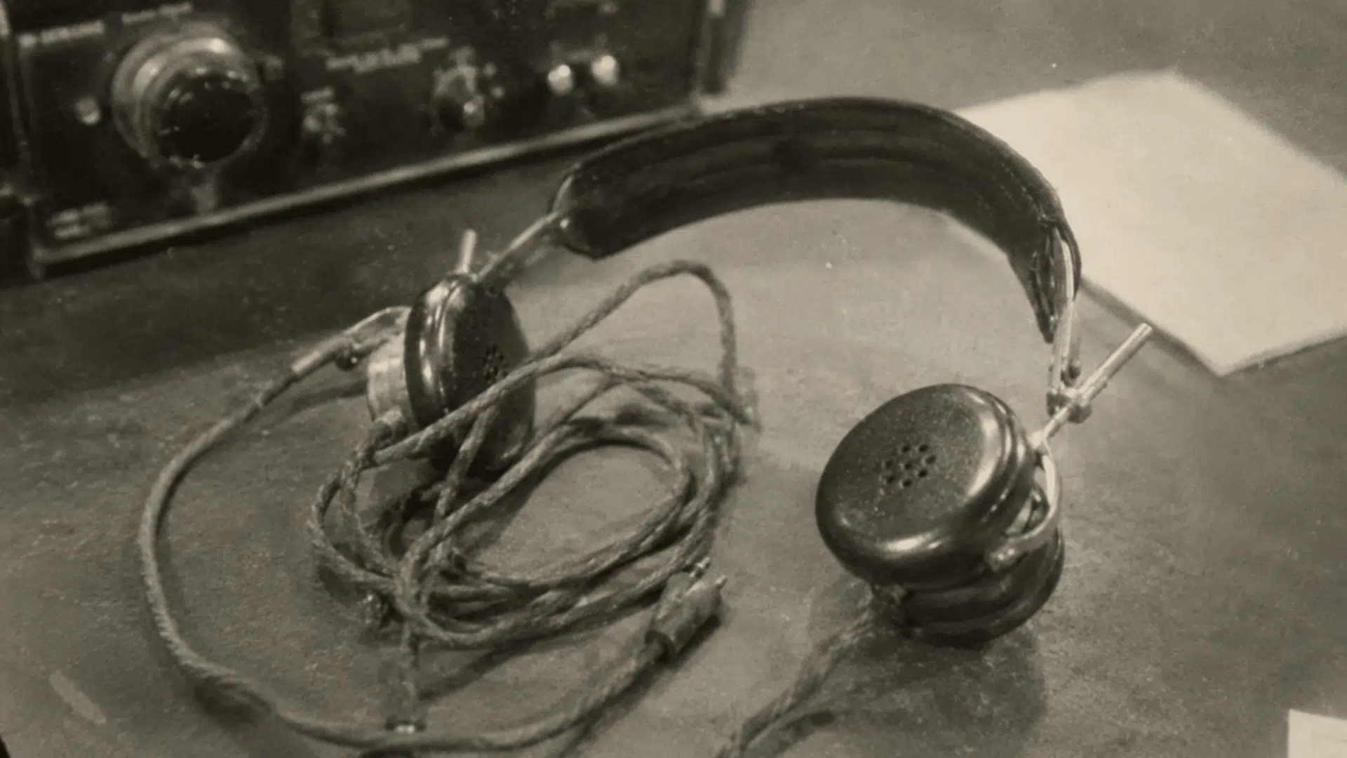 vintage radio communication headphones from the 1930s on a desk in a grainy black and white archival photo
