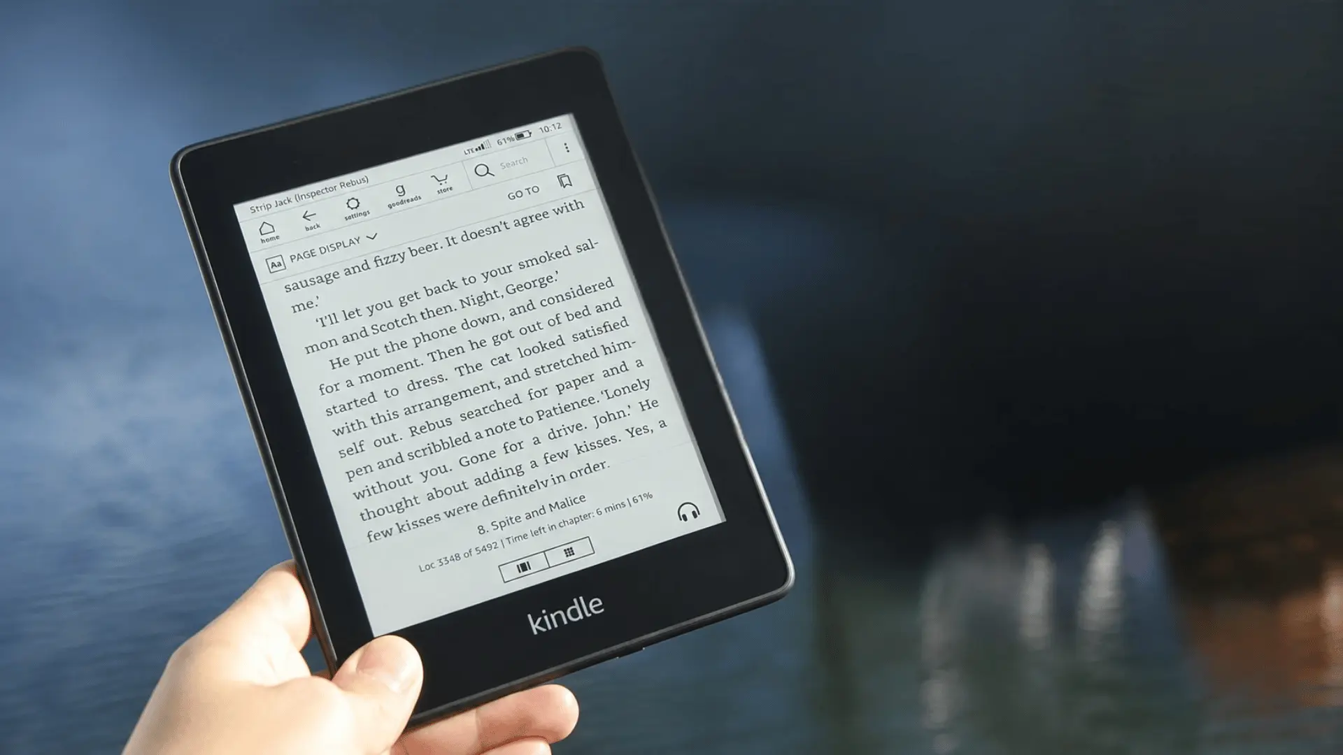 Black e-reader held in one hand with boats and water in the background