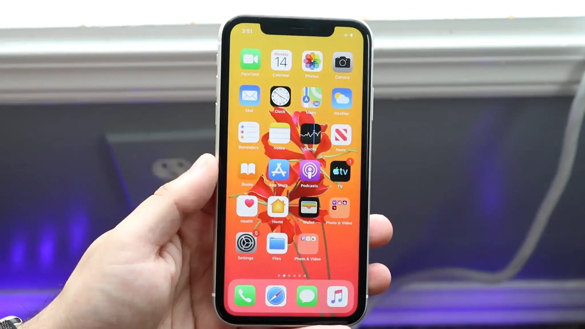 Hand holding an iPhone displaying the Home Screen with app icons and a visible screen notch.