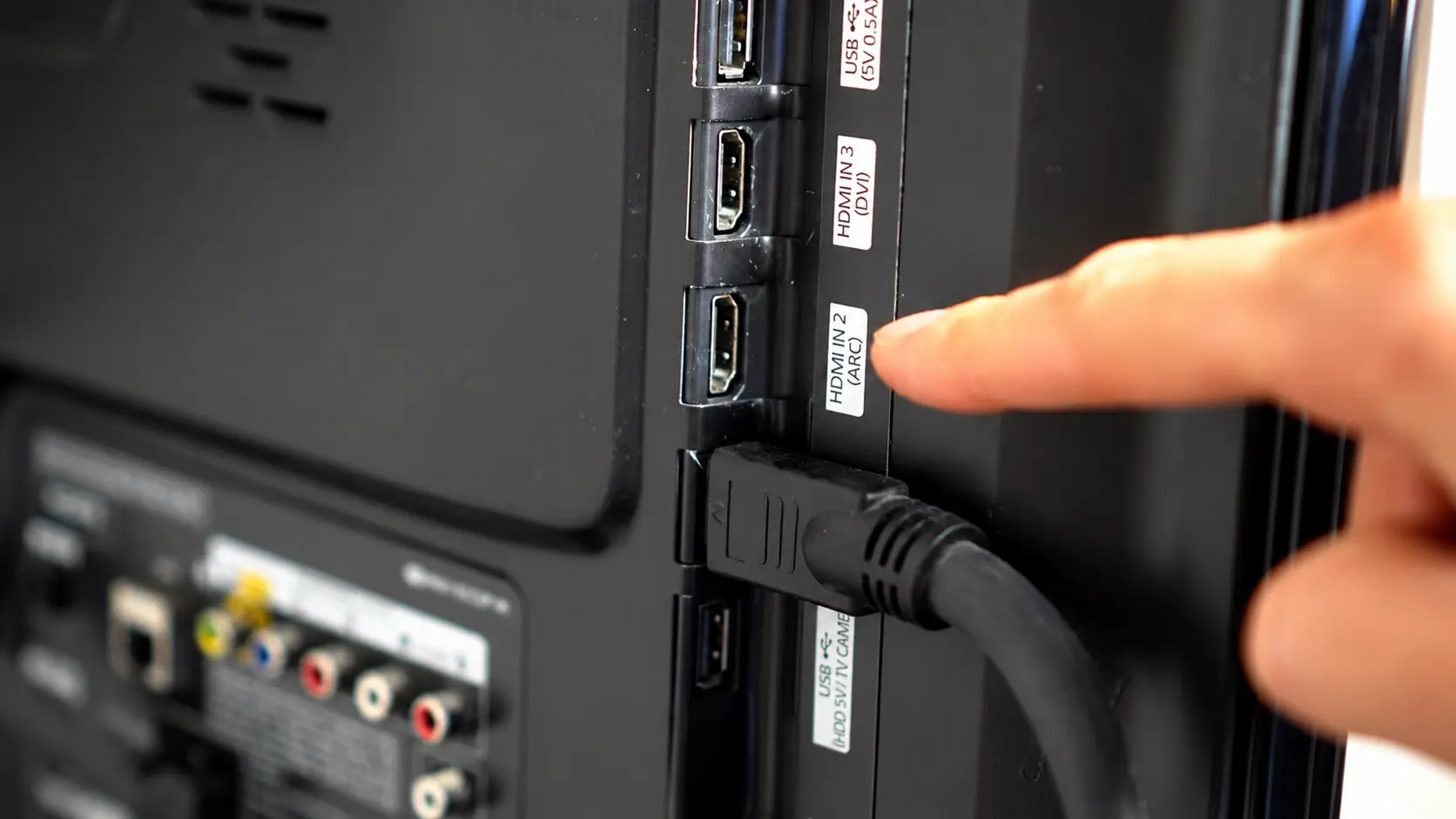 Close-up of HDMI ports on the back of a TV with an HDMI cable connected and a finger pointing to HDMI IN 2