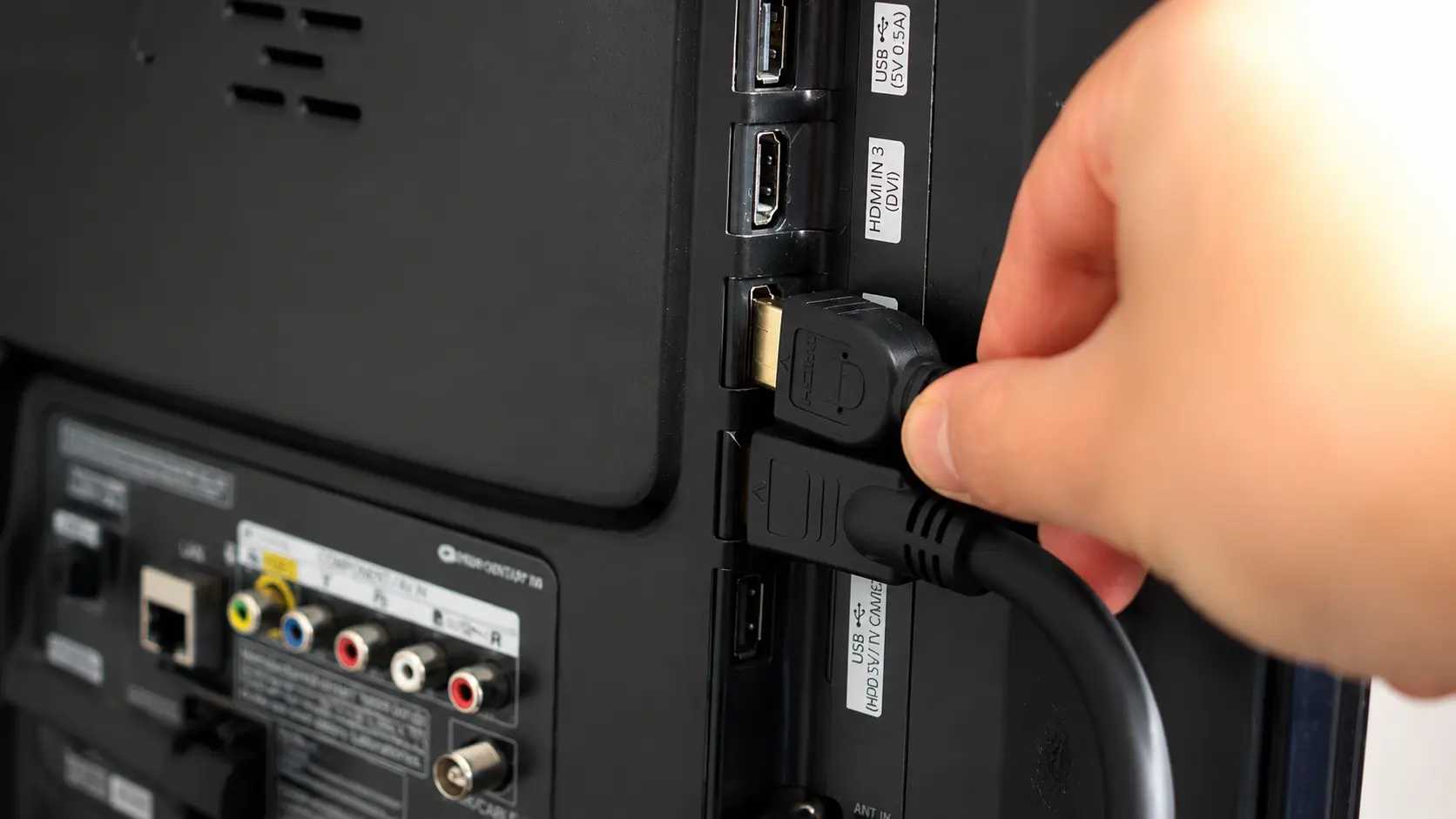 Close-up of a hand plugging an HDMI cable into the HDMI IN 2 port on the back of a TV