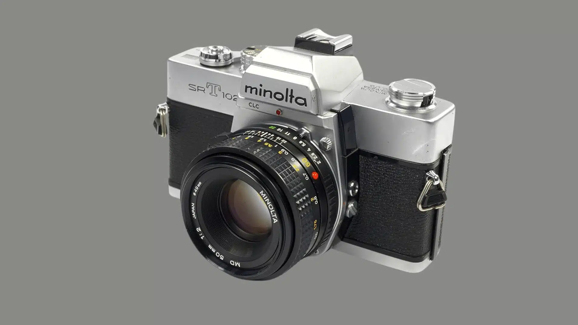 Three-quarter view of a silver and black Minolta SRT 102 film camera with a 50mm lens on a white background.