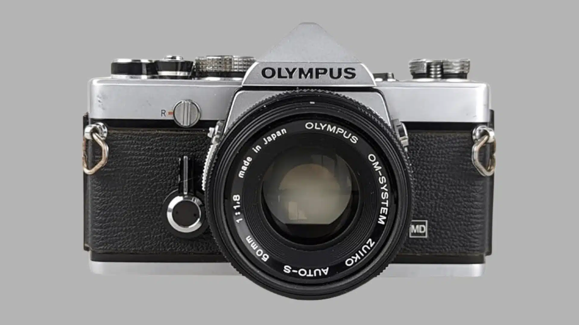 Front view of a silver and black Olympus OM film camera with a 50mm lens on a white background.