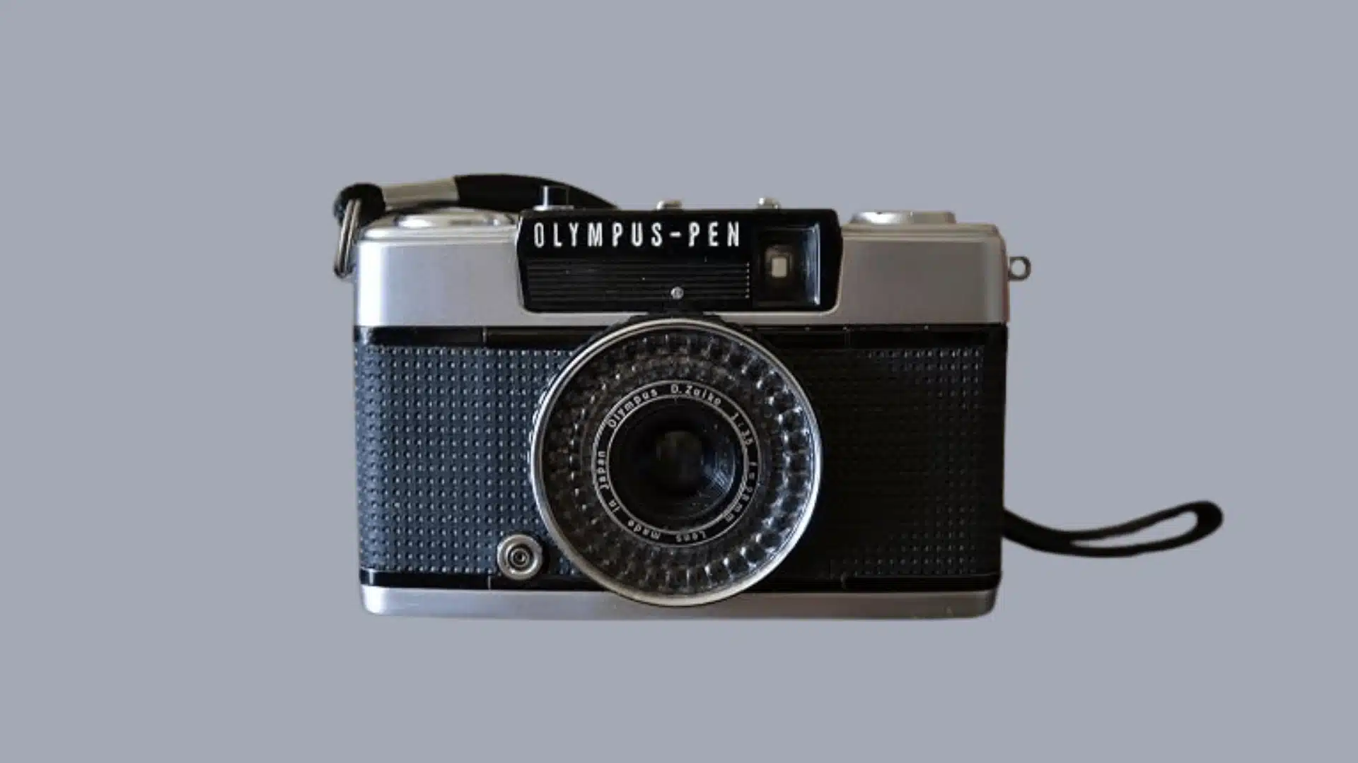 Front view of a silver and black Olympus Pen half-frame film camera resting on a dark table.