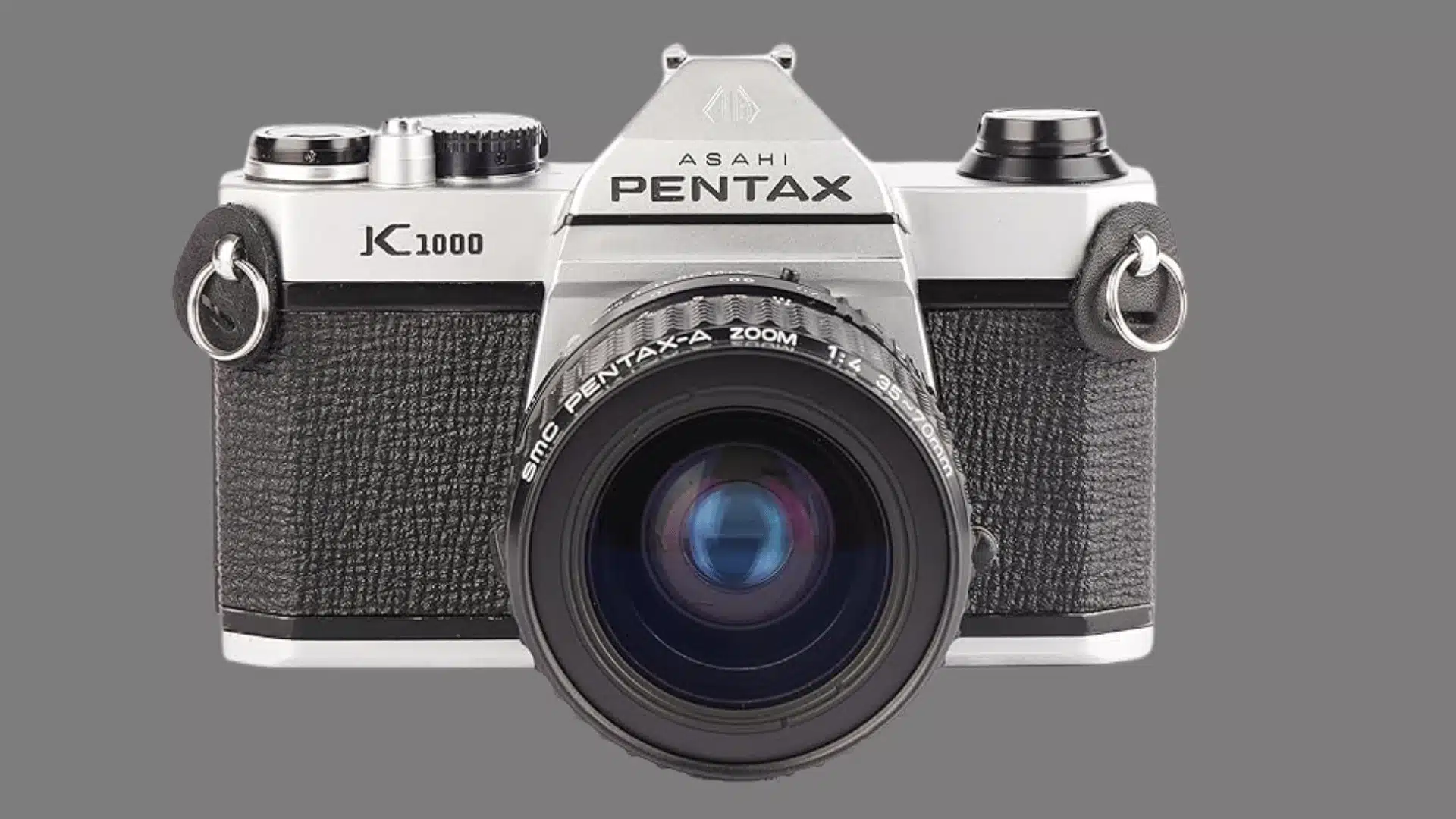 Front view of a silver and black Pentax K1000 film camera with a zoom lens on a white background.