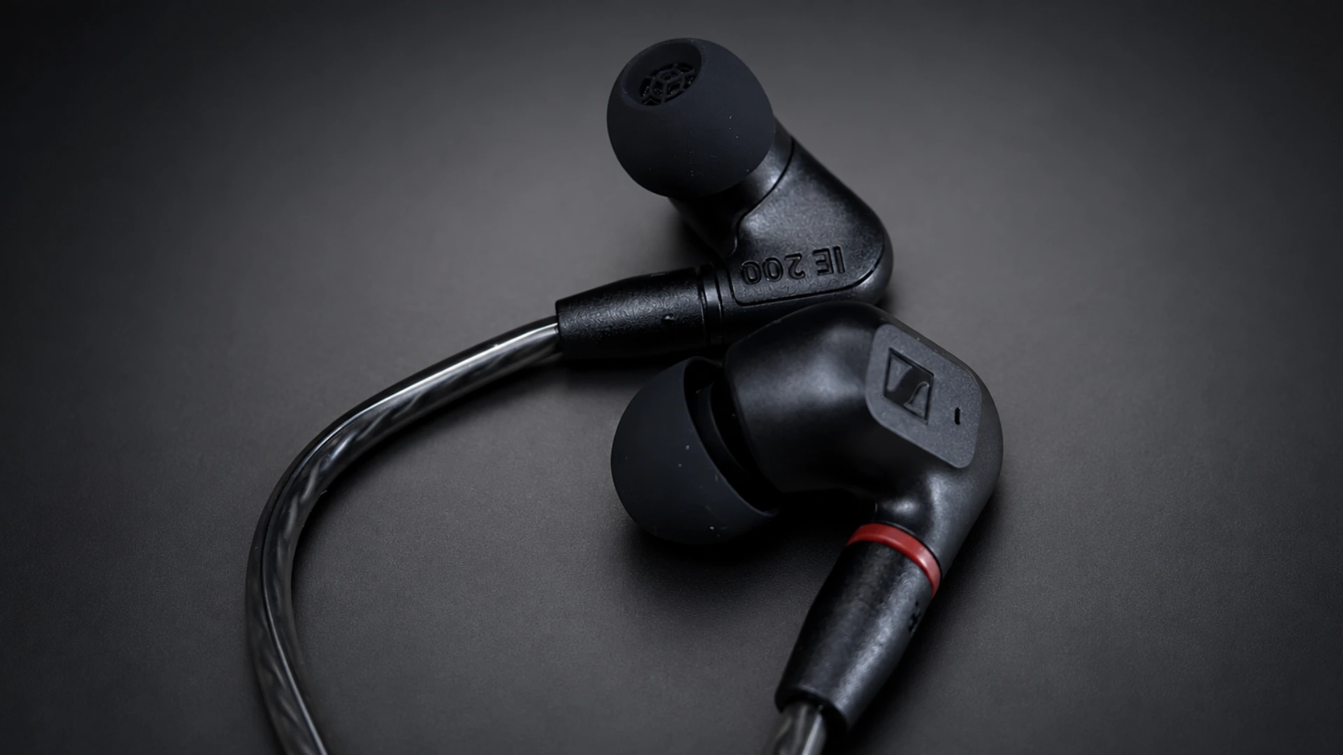 Black IE 200 wired earbuds and curved cable displayed on a dark gray studio background