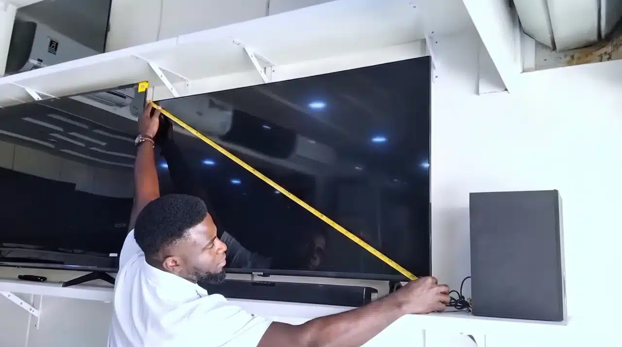 Man measures a large TV diagonally from the top-left to bottom-right screen corner with a tape measure.